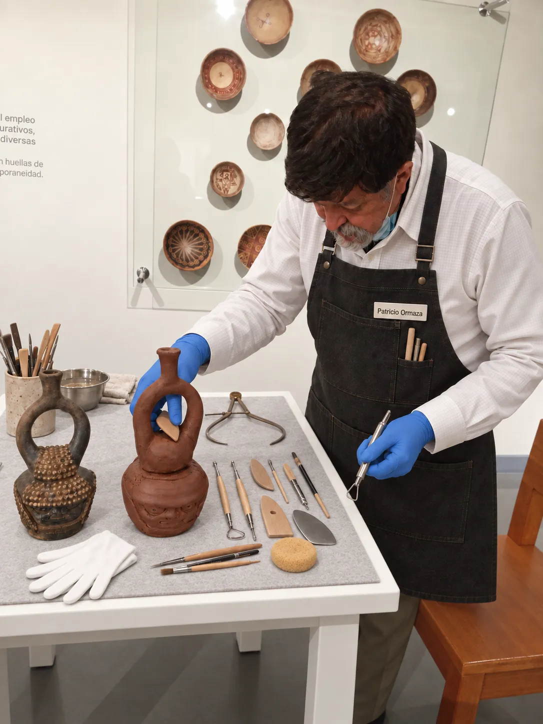 Persona modelando una reproducción de la botella de Palanda junto a la pieza original en un museo de Quito